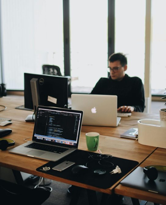 A web developer working on code in a modern office setting with multiple devices.